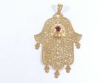 un pendentif en forme de hamsa en or, orné d'une pierre rouge au centre