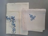 Trois serviettes blanches ornées de fleurs bleues sont posées sur une table.