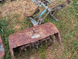 Plusieurs vieux outils agricoles sont posés dans l'herbe, à même le sol.