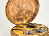 a gold pocket watch with gears on it on a white surface