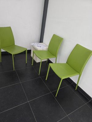 Trois chaises vertes sont alignées contre un mur blanc dans une salle d'attente