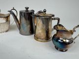 three silver teapots and a coffee pot on a white surface