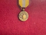 une médaille d'or posée sur un tissu rouge, accompagnée d'un ruban doré
