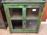 une vieille armoire verte avec des portes vitrées et des étagères, dans une pièce