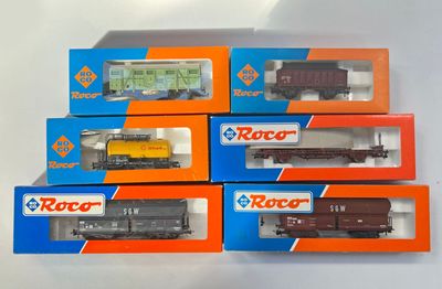 six boîtes contenant des trains miniatures, posées sur une surface blanche