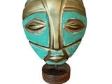 une image représentant un masque en or et turquoise posé sur un socle en bois