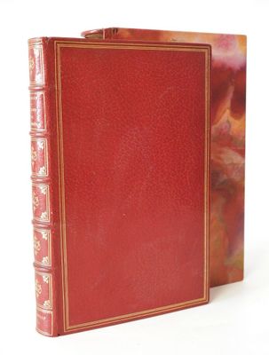 an old red book with gold trim sitting on top of a white surface