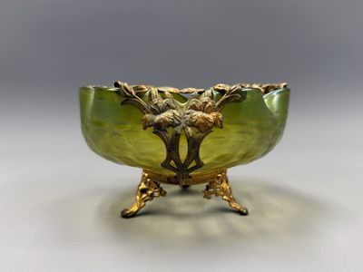 une image représentant un bol en verre vert posé sur un socle en métal
