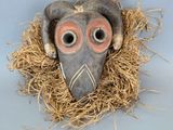 un masque d'oiseau en argile posé sur un lit de paille