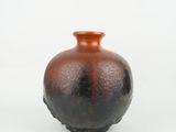 un petit vase brun posé sur une surface blanche