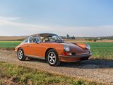 an orange porsche parked on the side of a dirt road next to a field