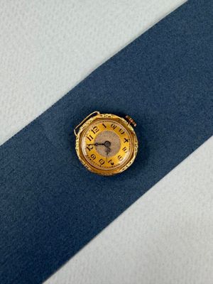 une montre en or posée sur une cravate bleue, sur une surface blanche