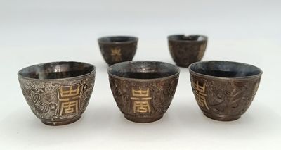 four silver cups are lined up in a row on a white surface