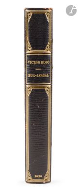 an old book with a black cover sitting on top of a white surface