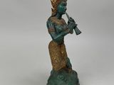 bronze statue of a woman playing a flute on a rock