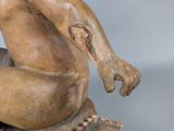 statue of a naked man sitting on a rock with his hands in the air