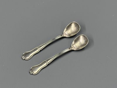 two silver spoons sitting on top of a table next to each other