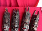 four wooden masks are lined up on a red cloth