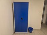 une porte bleue dans une pièce où se trouve un seau par terre