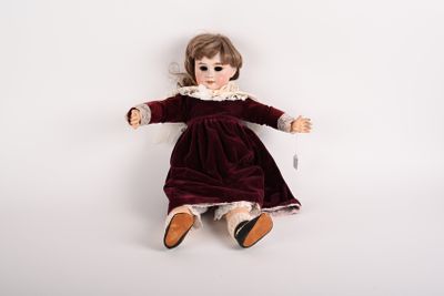 une poupée à l'ancienne, assise sur une surface blanche, vêtue d'une robe rouge
