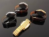 three watches are sitting on a black surface with a gold band