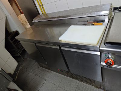 un plan de travail en acier inoxydable dans une cuisine professionnelle, sur lequel est posé une planche à découper
