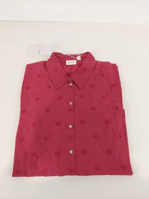 La chemise est rouge, ornée de cœurs, et possède un col boutonné.