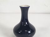 un petit vase noir posé sur une surface blanche