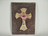 croix en or ornée de pierres roses et bleues, posée sur un socle en pierre marron