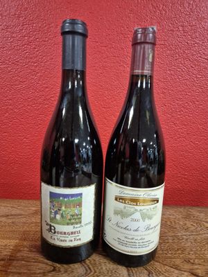 two bottles of wine sitting on top of a wooden table next to a red wall