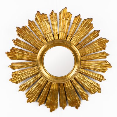 une photo d'un miroir doré en forme de soleil rayonnant accroché à un mur blanc