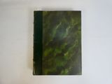 un vieux livre à la couverture verte posé sur une table blanche