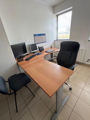 a desk with two computers and a chair in the corner