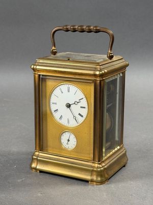 a gold clock with a handle on a gray surface