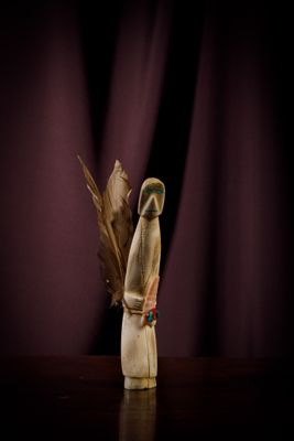 a small wooden figurine with a feather on a table