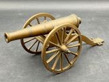 un canon doré posé sur un chariot en bois, sur une surface grise