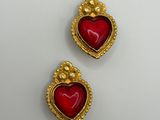 a pair of gold and red heart shaped earrings on a white surface