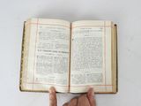 someone is holding an open book in their hand on a white surface