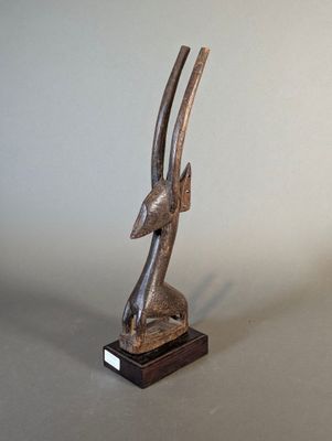 statue d'une antilope posée sur un socle en bois, sur fond gris