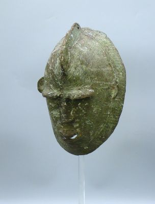 un masque antique en bronze posé sur un socle, sur fond gris