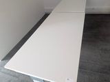 une table blanche dans une pièce où se trouve un tableau noir accroché au mur