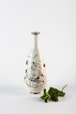 un vase blanc orné d'un motif noir et blanc, à côté d'une feuille verte