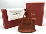 un sac à main marron posé à côté d'une boîte rouge sur une surface blanche