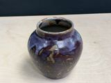 a purple vase sitting on a table with a black wall in the background