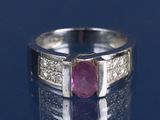 une photo d'une bague sertie d'un rubis et de diamants posée sur une surface réfléchissante