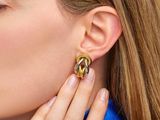 La femme porte une paire de boucles d'oreilles en or et une chemise bleue.