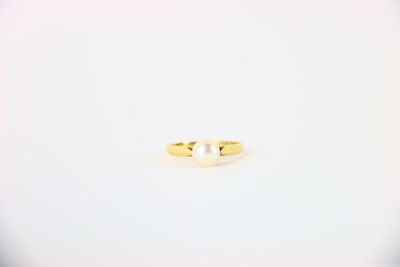 une bague en or sertie d'une perle, posée sur un fond blanc