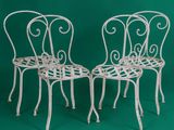 two white wrought chairs against a green background