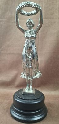 statue en argent représentant une femme tenant une bague, posée sur un socle en bois