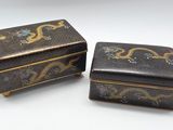 une paire de boîtes décorées de noir et d'or posées sur une surface blanche